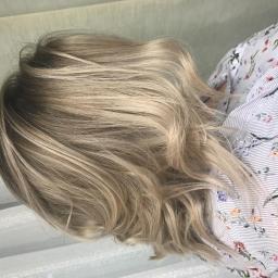 Salon Look Fryzjersko-Kosmetyczny - Świeżo wystylizowane, blond włosy z delikatnymi falami, widoczne w jasnym oświetleniu, z bluzką w kwiaty w tle.