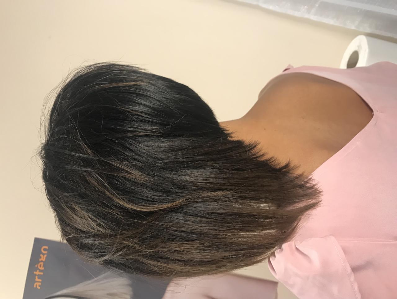 Krótkie, ciemne włosy z jaśniejszymi pasemkami, świeżo po strzyżeniu, widok z tyłu na szyję i ramiona kobiety w różowej bluzce.