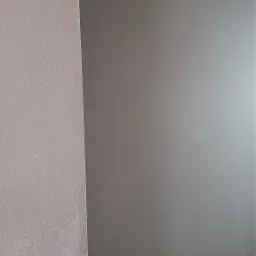 Świeżo nałożony, gładki tynk maszynowy na ścianie, w odcieniach szarości, z widoczną strukturą na sąsiedniej ścianie po lewej stronie.