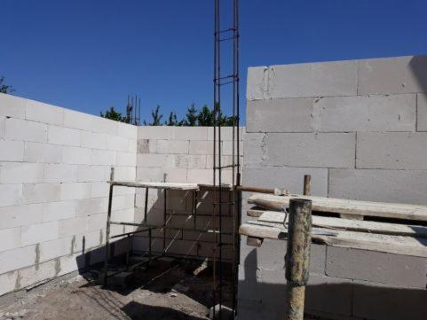 Wznoszenie ścian z białych bloczków z betonu komórkowego, widoczne zbrojenie pionowe i rusztowanie robocze, etap budowy domu jednorodzinnego.