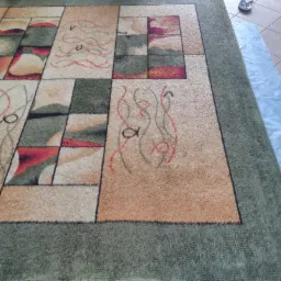 Wzór geometryczny na dywanie z motywem ryb, częściowo przykryty folią ochronną podczas czyszczenia.