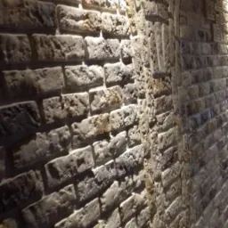 Dekoracyjna ściana z cegły w odcieniach szarości i beżu, oświetlona punktowo, z widocznym łukowatym przejściem.