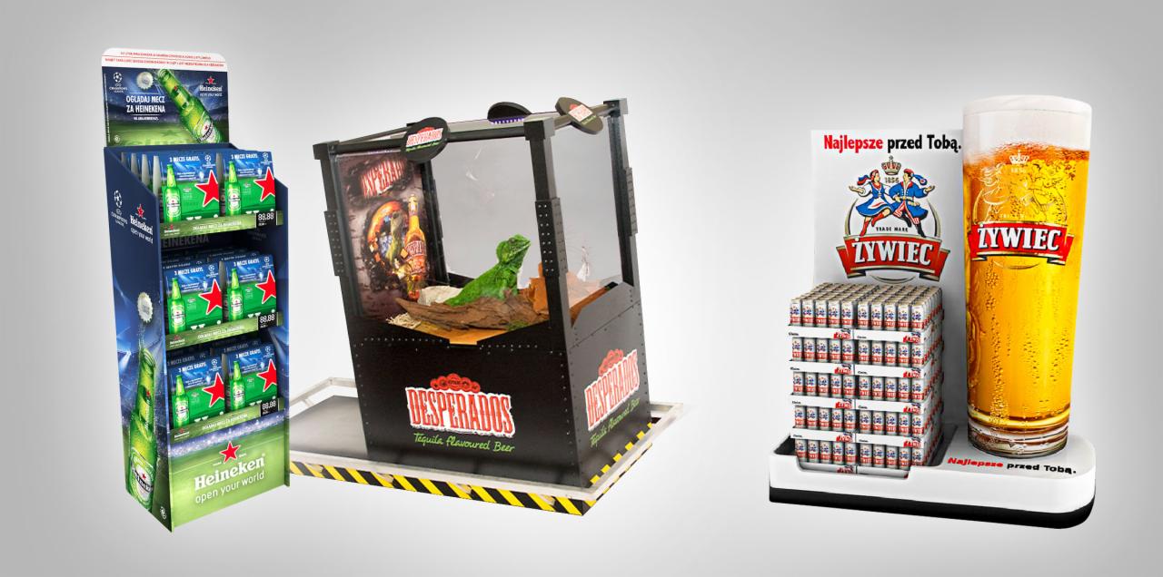 Ekspozytory reklamowe różnych marek piwa: Heineken z piłkarskim motywem, Desperados z jaszczurką w dioramie oraz Żywiec z grafiką i stosem puszek.