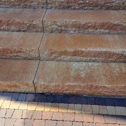 Mega Myjnia - Schody zewnętrzne z kostki brukowej w odcieniach brązu i beżu, prowadzące do budynku z białym elementem elewacji, widoczne z bliska z perspektywy lekko od dołu.