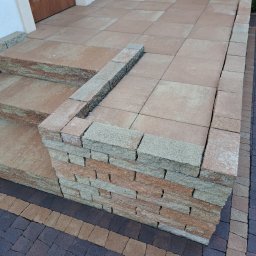 Mega Myjnia - Ułożone schody wejściowe z kostki brukowej w odcieniach beżu i brązu, z widocznym fragmentem chodnika z ciemnej kostki brukowej w tle.