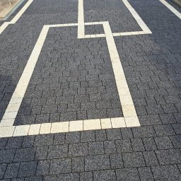 Mega Myjnia - Szara kostka brukowa z geometrycznym wzorem z jasnych kostek, tworzącym kwadraty i linie. Widok z góry, równomierne oświetlenie.