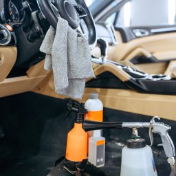 Mega Myjnia - Wnętrze auta z beżową tapicerką, ściereczka na kierownicy i preparaty do czyszczenia dywaników, detaling samochodowy.