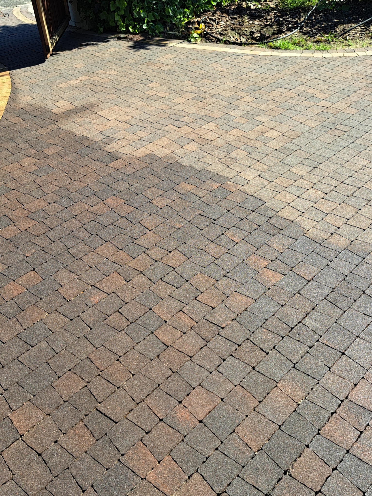 Częściowo umyta kostka brukowa w odcieniach brązu i szarości, widoczna różnica w kolorze między czystą a zabrudzoną powierzchnią, z fragmentem roślinności w tle.