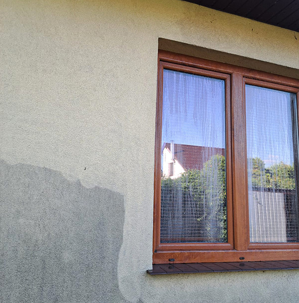 Fragment elewacji budynku z oknem, ukazujący obszar po czyszczeniu. Widoczne różnice w odcieniu i strukturze tynku przed i po zabiegu.