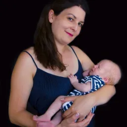 Portret kobiety w granatowej sukience trzymającej na rękach śpiącego niemowlaka w pasiastym ubranku na czarnym tle.