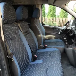 Wnętrze busa z trzema fotelami obitymi niebiesko-czarną tapicerką w kropki, widok z boku na przednie siedzenia i deskę rozdzielczą.