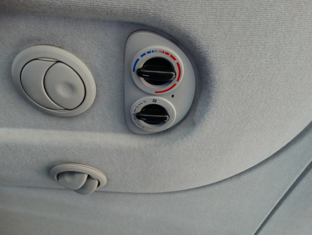 Wnętrze pojazdu: nawiewy i panel sterowania klimatyzacją w podsufitce z szarej tapicerki.