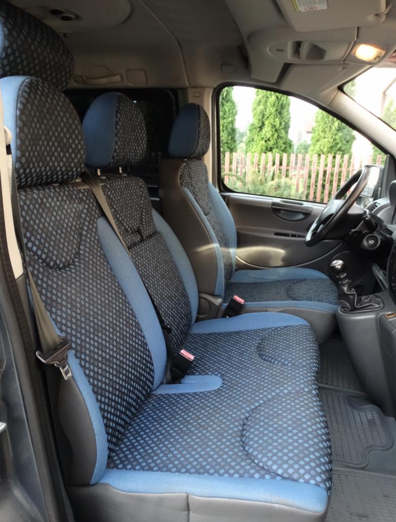 Wnętrze busa z trzema fotelami obitymi niebiesko-czarną tapicerką w kropki, widok z boku na przednie siedzenia i deskę rozdzielczą.