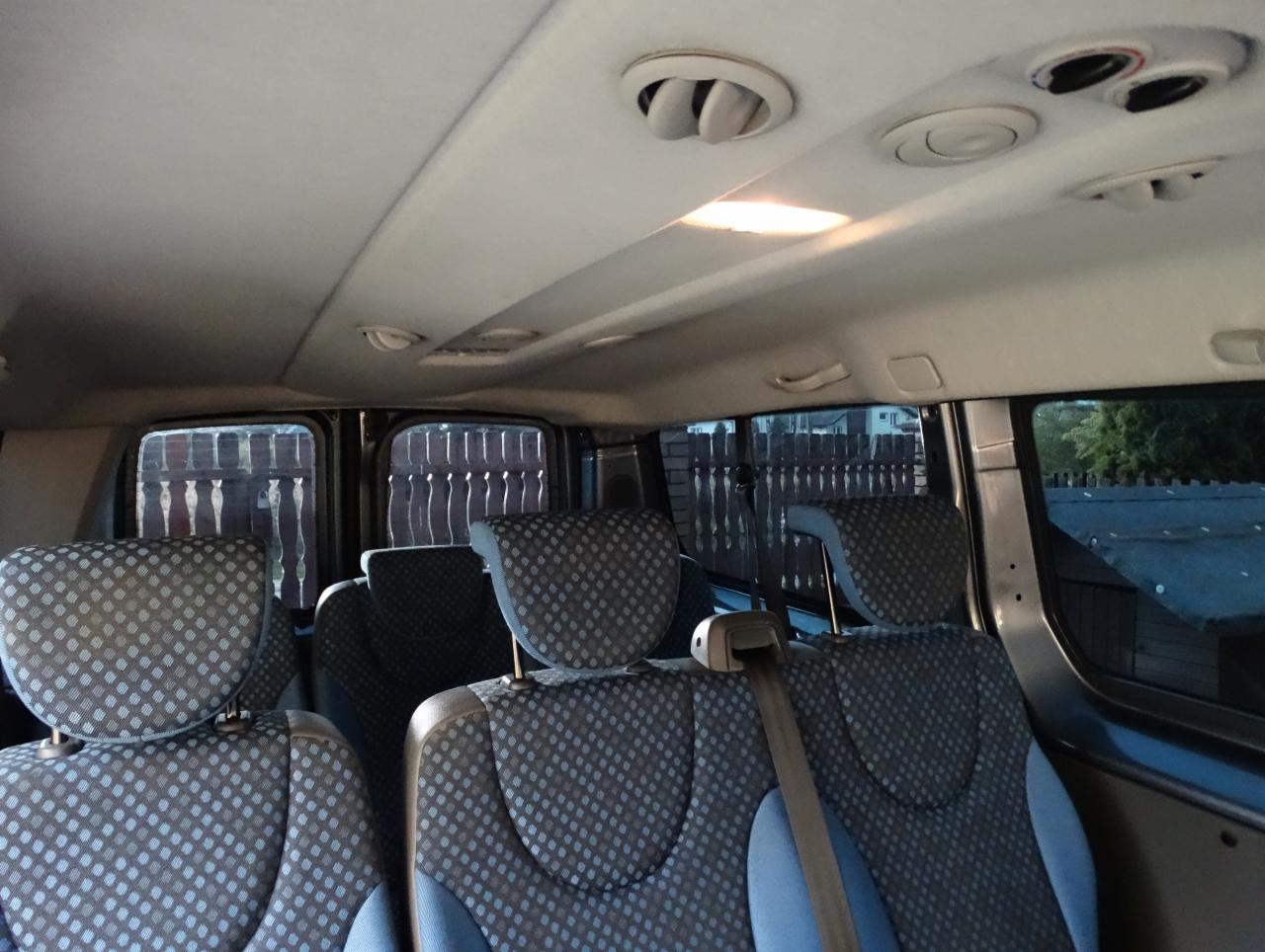 Wnętrze busa pasażerskiego z szarymi fotelami w niebieskie kropki, widok z tyłu pojazdu.