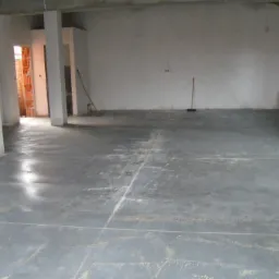 Świeżo wylana, szara posadzka jastrychowa w surowym wnętrzu budynku w Pruszkowie, widoczne ślady po wylewce i częściowo zacieraniu.