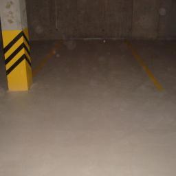 Rut-Bud - Gładka, szara posadzka w hali garażowej z żółtymi liniami wyznaczającymi miejsca parkingowe i słupem oznaczonym czarno-żółtymi pasami ostrzegawczymi.