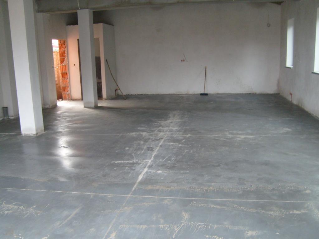 Świeżo wylana, szara posadzka jastrychowa w surowym wnętrzu budynku w Pruszkowie, widoczne ślady po wylewce i częściowo zacieraniu.