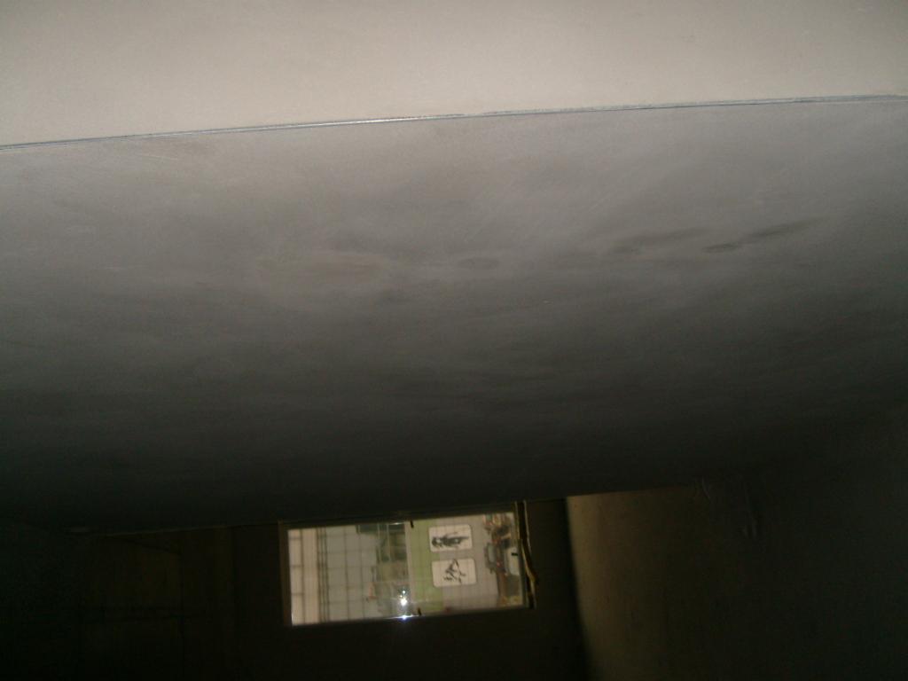 Szpachlowana, surowa powierzchnia sufitu w pomieszczeniu z widocznym oknem i niedoskonałościami w wykończeniu.