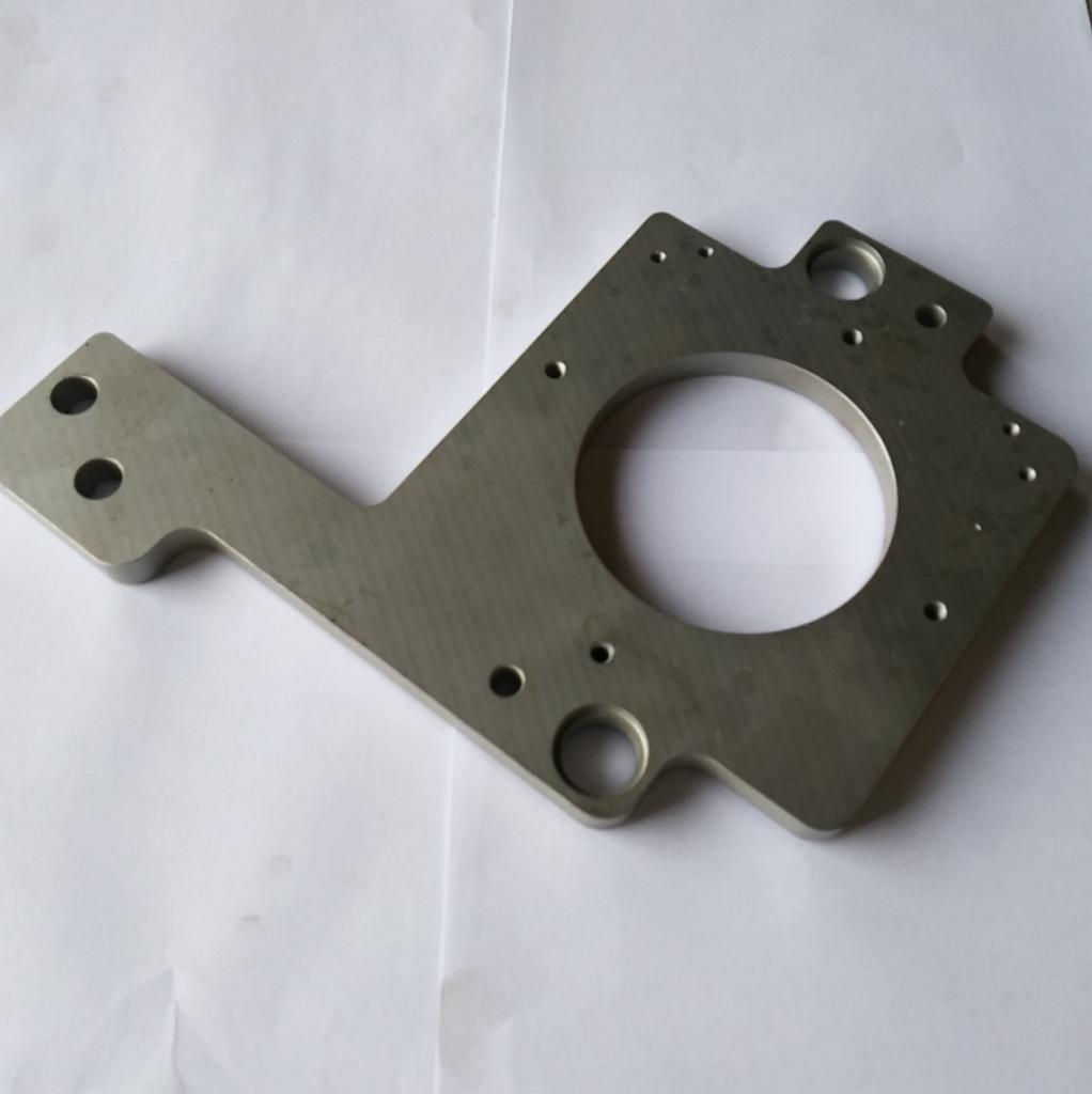 Precyzyjnie wycięty, metalowy element o nieregularnym kształcie z licznymi otworami, leżący na białym tle.