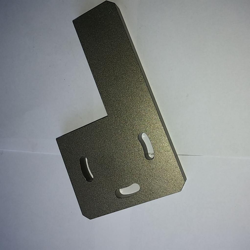 Metalowy kątownik z trzema owalnymi otworami, wykończony szorstką, ciemnoszarą powłoką, leżący na białym tle.