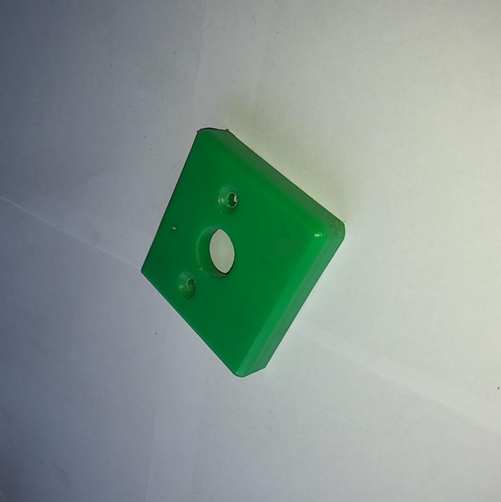 Jaskrawozielona, kwadratowa płytka z tworzywa sztucznego z trzema otworami (dwa małe, jeden większy) leżąca na białym tle, wykonana prawdopodobnie metodą obróbki CNC.