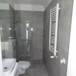 Mar-bud - Nowoczesna łazienka z szarymi płytkami, kabiną prysznicową ze szklaną ścianką i białym grzejnikiem drabinkowym.