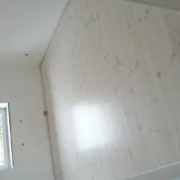 Jasne, bielone deski podłogowe w nowym pomieszczeniu z widocznym oknem i świeżo pomalowanymi ścianami, widoczne ślady po szpachlowaniu i montażu.