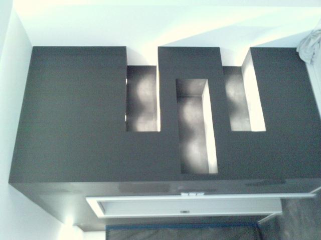 Grafitowa zabudowa sufitowa z geometrycznymi wnękami, podświetlona od wewnątrz, z widocznym fragmentem wentylacji.