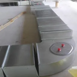 Elementy kanałów wentylacyjnych, z widocznymi czerwonymi pokrętłami regulacyjnymi, ułożone na podłodze surowego wnętrza w trakcie montażu.