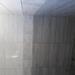 Mirex Bud - Ściana wyłożona jasnymi i ciemnymi płytkami imitującymi drewno, z dekoracyjnym pasem płytek w kwiatowy wzór.