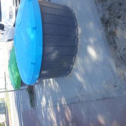 Mirex Bud - Dwa plastikowe pojemniki na śmieci z niebieską i zieloną pokrywą stojące na chodniku z kostki brukowej, w tle zaparkowany biały samochód dostawczy.