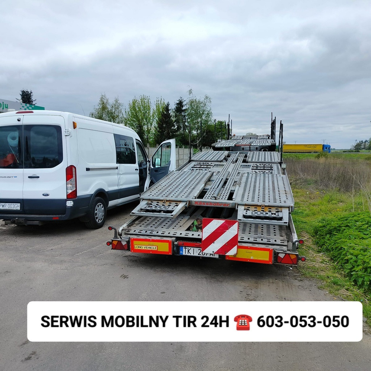 Biały bus Ford Transit z otwartymi drzwiami obok dwupoziomowej, pustej lawety marki Kassbohrer; w tle widoczny żółty samochód ciężarowy z naczepą.