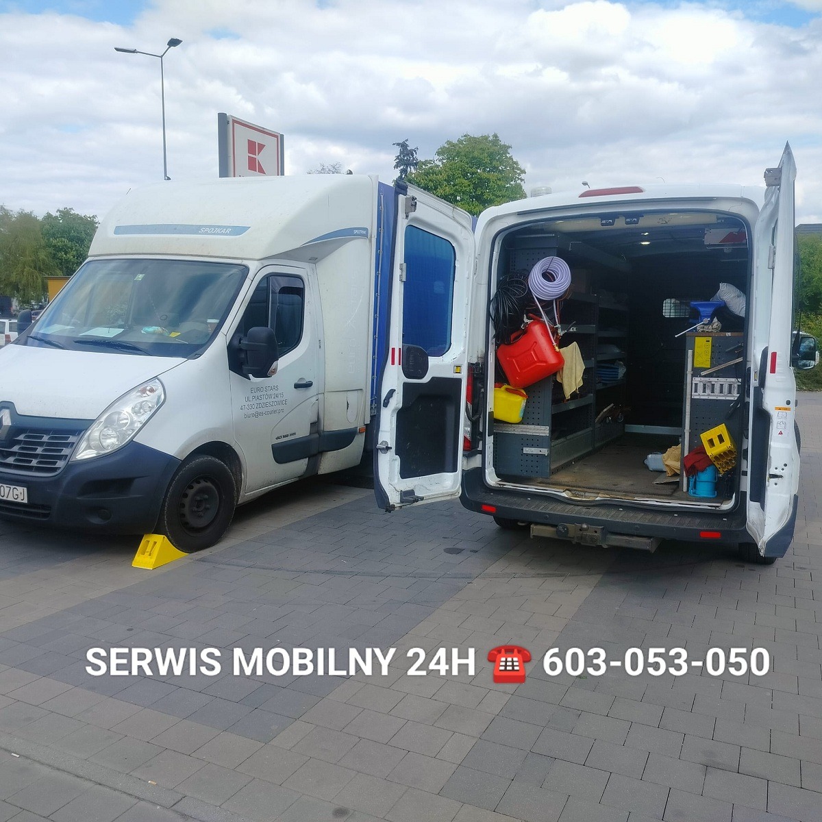 Dwa białe busy zaparkowane na kostce brukowej, z otwartymi drzwiami. Jeden bus z podniesioną plandeką, drugi z widocznym wyposażeniem serwisowym wewnątrz, w tym kanister, węże i narzędzia. Żółte...