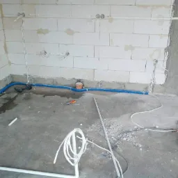 Wnętrze w trakcie prac instalacyjnych: widoczne przewody elektryczne prowadzone po ścianach z betonu komórkowego i w podłodze, narzędzia oraz skrzynka narzędziowa na posadzce.