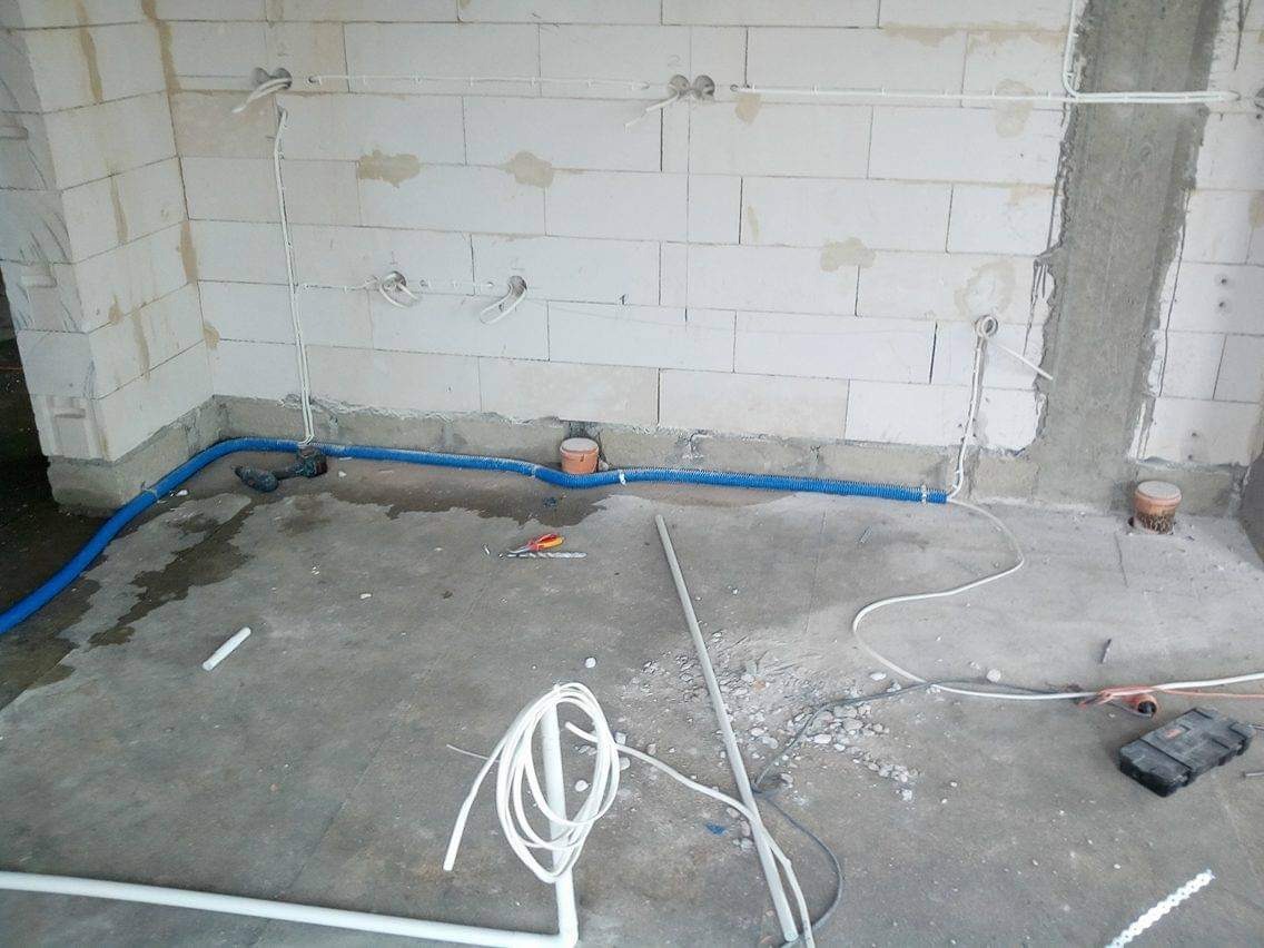 Wnętrze w trakcie prac instalacyjnych: widoczne przewody elektryczne prowadzone po ścianach z betonu komórkowego i w podłodze, narzędzia oraz skrzynka narzędziowa na posadzce.