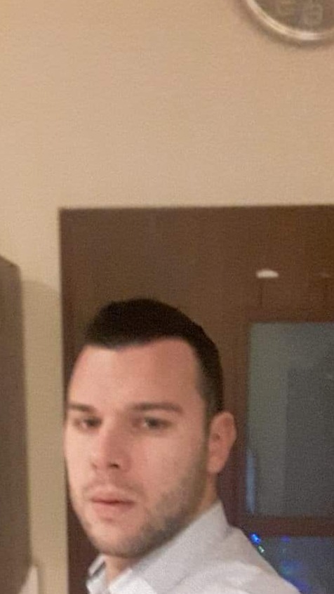 Portret mężczyzny w koszuli na tle ściany z zegarem.