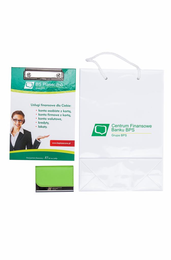 Zestaw gadżetów reklamowych Banku BPS Piaseczno: notes, torba papierowa, podkładka z klipsem, prezentujące logo i ofertę usług finansowych.