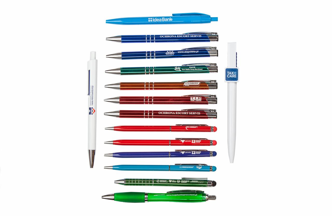 Zestaw kolorowych długopisów reklamowych z nadrukami różnych firm, ułożonych równolegle na białym tle.
