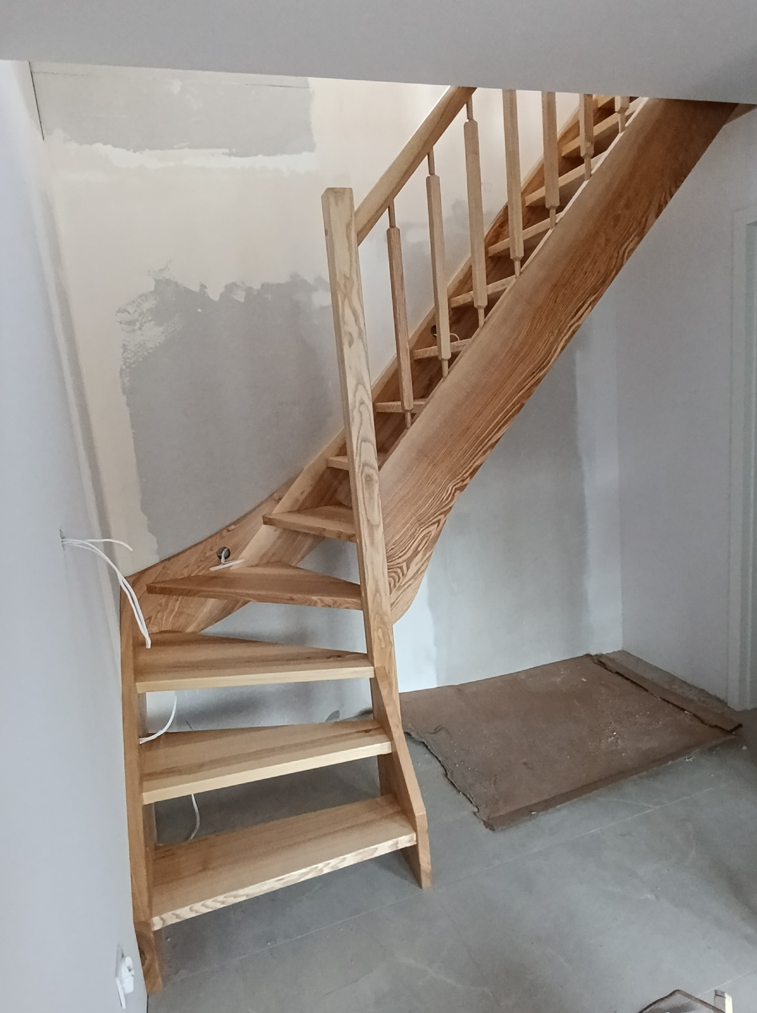 Jasne, drewniane schody z balustradą w trakcie montażu w Międzyrzeczu. Widoczne niedokończone ściany i surowy stan wykończenia wnętrza. Naturalne oświetlenie.