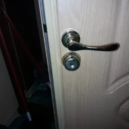 Drzwi wewnętrzne z zamontowaną klamką i zamkiem. W tle widoczny fragment wiadra i mopa.