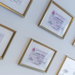 Ściana gabinetu z ramkami zawierającymi certyfikaty ukończenia kursów refleksologii, w złotych ramkach, z nazwiskiem Agnieszka Przybysz.