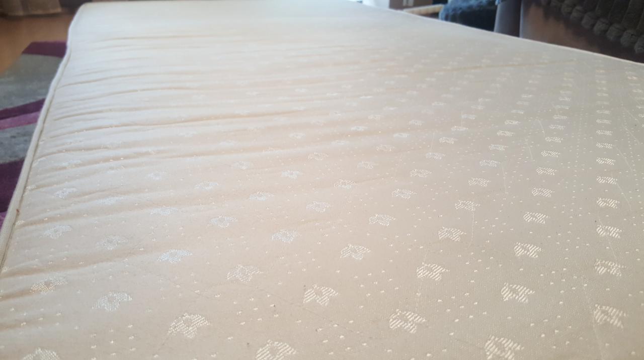 Beżowy materac z delikatnym wzorem liści i kropek, leżący na podłodze z dywanem w tle.
