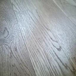 Ukośnie ułożone panele podłogowe w odcieniach szarości i beżu, imitujące naturalne drewno z wyraźnym rysunkiem słojów, widoczne łączenia paneli.