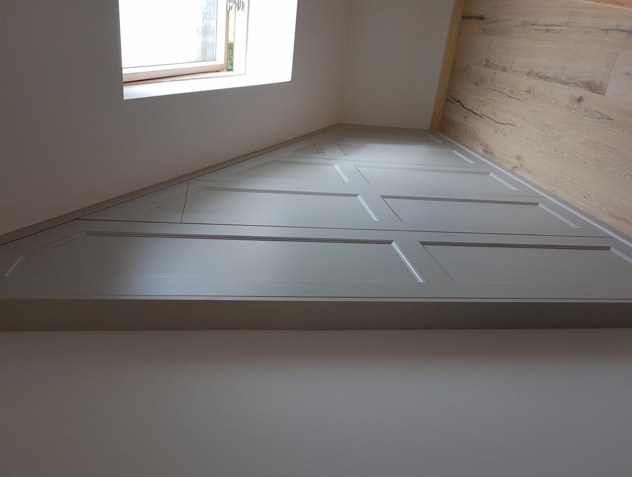 Zabudowa wnęki pod skosem na poddaszu, szare, frezowane fronty szafek, drewniana podłoga, małe okno dachowe.