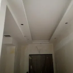 Sufit podwieszany z płyt kartonowo-gipsowych z widocznymi otworami na oświetlenie, surowe ściany w trakcie wykończenia, widoczne przewody elektryczne.