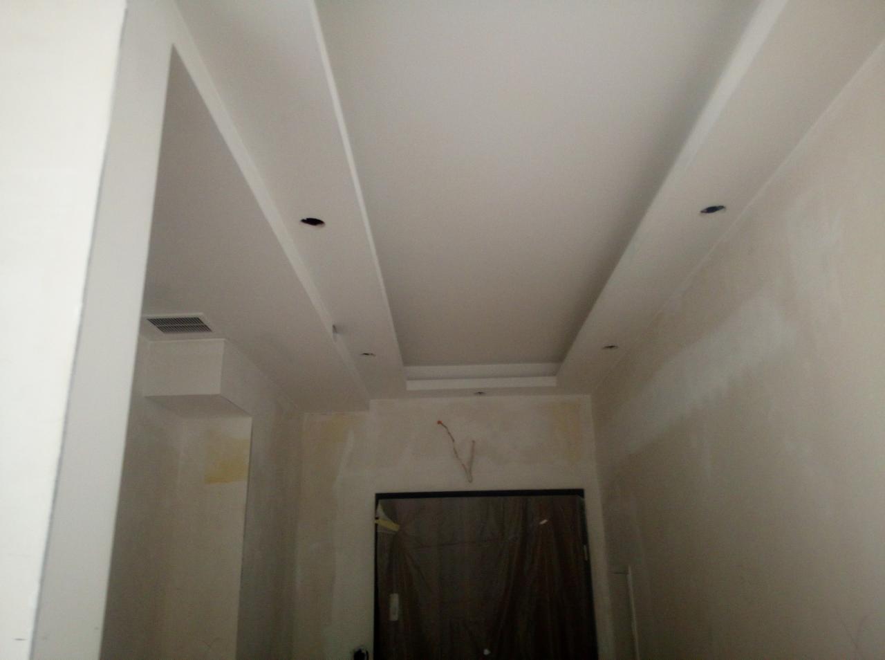 Sufit podwieszany z płyt kartonowo-gipsowych z widocznymi otworami na oświetlenie, surowe ściany w trakcie wykończenia, widoczne przewody elektryczne.