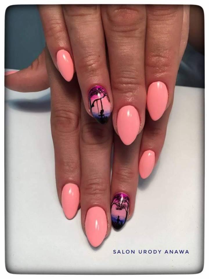 Ręce z pomalowanymi na różowo paznokciami w kształcie migdała, na dwóch paznokciach namalowany krajobraz z palmami i huśtawką na tle zachodzącego słońca.