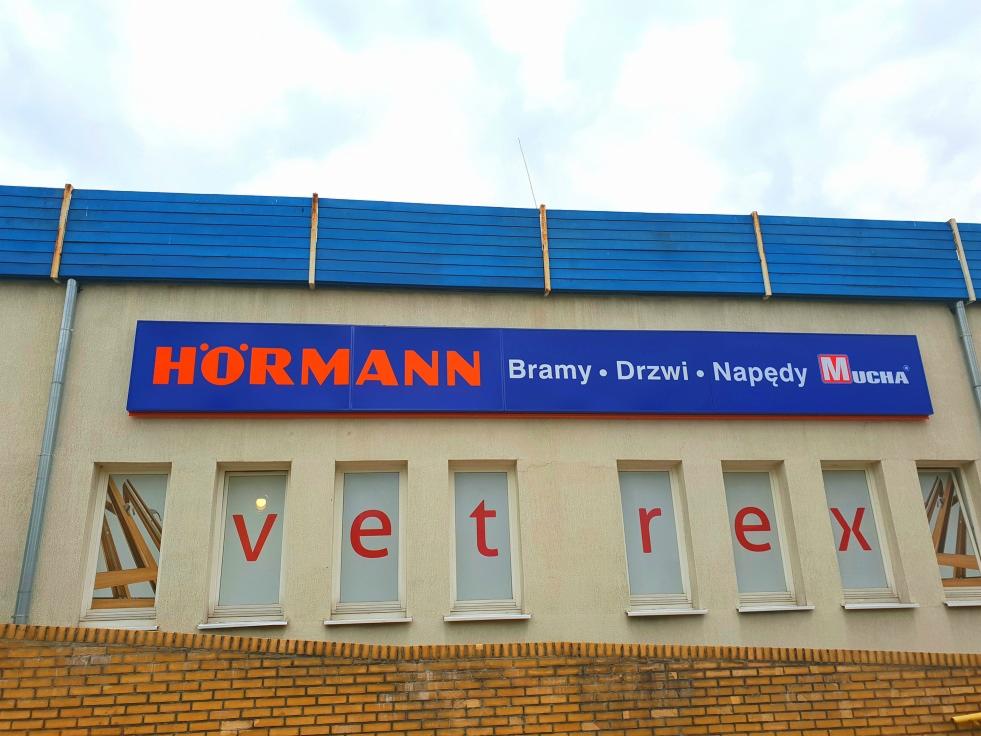 Budynek firmy VETREX z szyldem HÖRMANN, oferującej bramy, drzwi i napędy, z oknami z literami układającymi się w nazwę firmy.