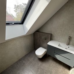 Krasa Krystian - Nowoczesna łazienka na poddaszu z dużym oknem dachowym, szarymi płytkami lastryko na ścianach i podłodze, podwieszaną toaletą oraz szafką umywalkową w odcieniach szarości.