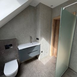 Krasa Krystian - Nowoczesna łazienka na poddaszu z szarymi płytkami lastryko na ścianach i podłodze, białym WC podwieszanym, ciemnoszarą szafką z umywalką i szklaną ścianką prysznicową.